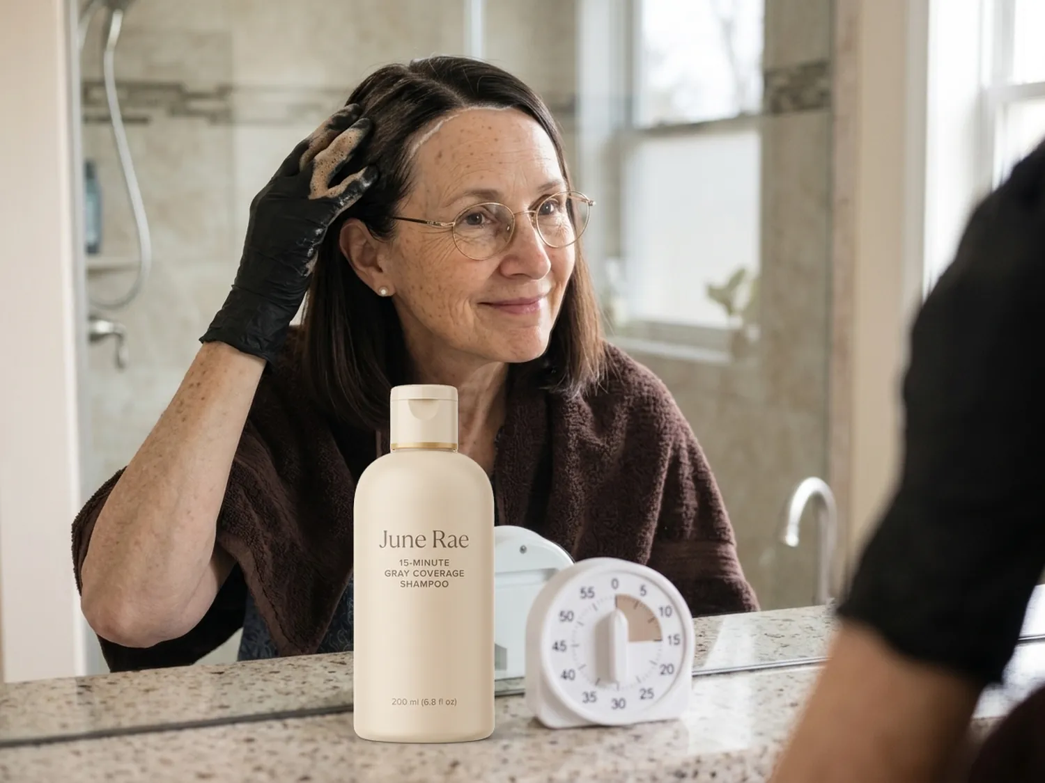 Peggy in black gloves working the shampoo into the white roots at her temples, the June Rae bottle and a timer beside her